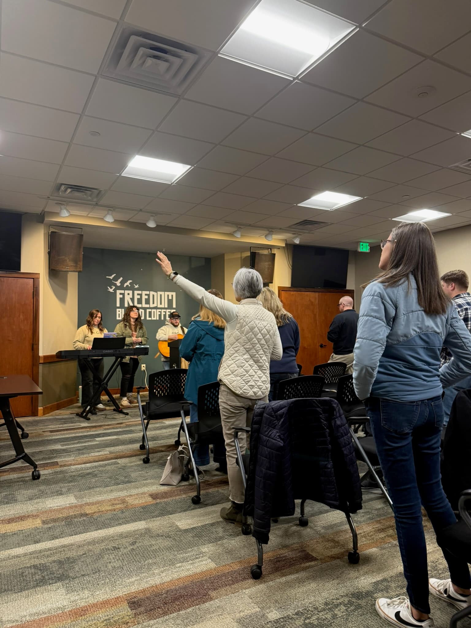 A woman in worship with hand raised during a gathering at Freedom Blend Coffee.